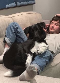 a man laying on top of a couch next to a black and white dog