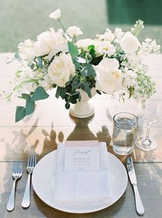 a table setting with white flowers in a vase and silverware on the place settings