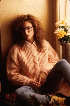 a woman sitting on the floor in front of a window wearing glasses and a sweater