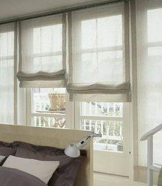 a bed sitting under two windows next to a window with blinds on top of it