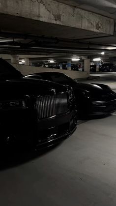 two black rolls royces are parked in a parking garage with no one around them