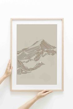 two hands holding up a framed photograph with mountains in the background and one hand reaching for it