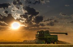 the sun is setting behind a green combineer in a wheat field with dark clouds