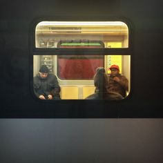 two people sitting on a train looking out the window at another person standing in front of them