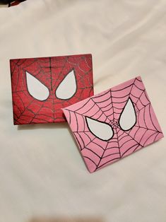 two pieces of paper with spider - man faces painted on them sitting on a bed