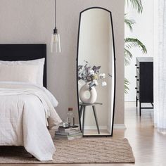 a bedroom with a bed, mirror and vase on the floor in front of it