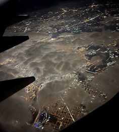 an aerial view of the city lights and clouds at night as seen from inside an airplane