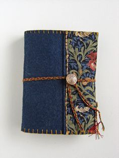 a small notebook covered in blue fabric with a button on the front and red string