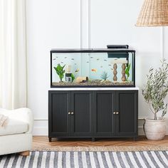 a fish tank sitting on top of a black cabinet next to a white couch and lamp