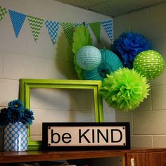 there is a sign that says be kind on the shelf next to some paper decorations