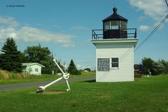 a white light house sitting on the side of a road next to a lush green field