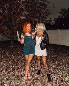 two women dressed in costumes standing next to each other on the ground with leaves all over them