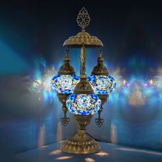 an ornate light fixture with blue and white glass on it's sides, in front of a brightly lit background