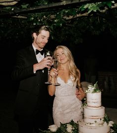 a man and woman standing next to each other holding wine glasses in front of a cake