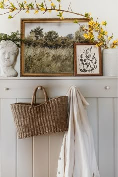 a basket hanging on the wall next to a painting and a vase with yellow flowers