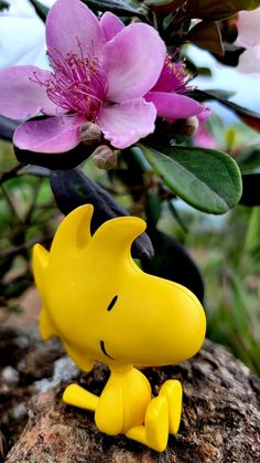 a small yellow dog figurine sitting on top of a rock next to a pink flower