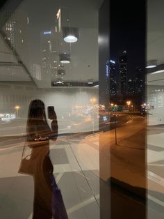 a woman taking a selfie in front of a window at night with the city lights behind her