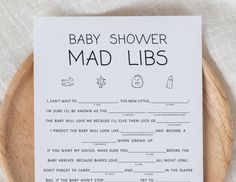 a baby shower mad libs game on a wooden plate with white linen and black lettering