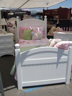 a white bed with pink and green pillows in a room filled with other bedspreads