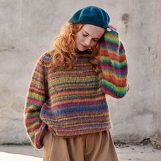 a woman with red hair wearing a multicolored sweater and green beret is talking on her cell phone