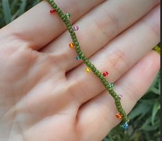 a hand holding a green beaded bracelet with multicolored beads on it's end