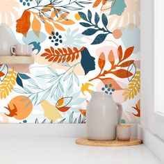 an orange and blue floral wallpaper with white vases on the counter next to it