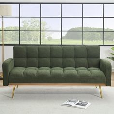 a green couch sitting in front of a window next to a book on the floor