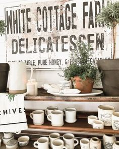 coffee cups and mugs are sitting on a table in front of a sign that says white cottage farm delicatessen