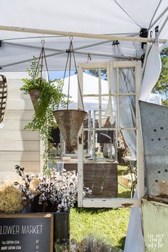 an outdoor market with flowers and plants hanging from it's sides under a white tent