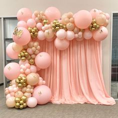 an arrangement of balloons and streamers are on display in front of a pink curtain