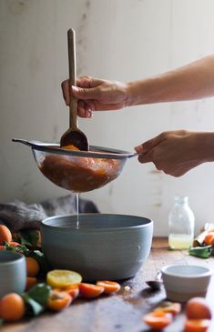 a woman is mixing oranges in a bowl with a wooden spoon on the table