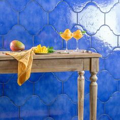 a table with fruit on it in front of a blue tile wall and wooden legs