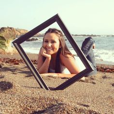 a woman laying in the sand with her hand on her chin and looking at the camera