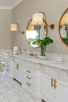 a large bathroom with marble counter tops and gold accents on the wall, along with two round mirrors