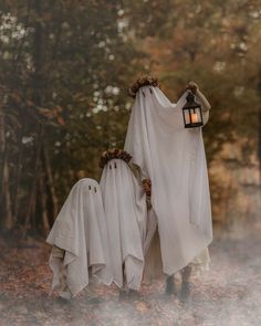 two ghostly people walking through the woods with their heads covered in white cloths and holding a lantern