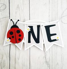 a ladybug banner with the word one hanging from it's side on a white wooden background