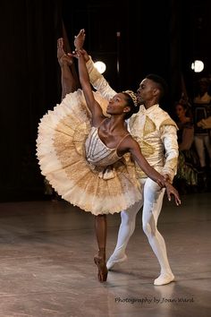 two ballerinas in white and gold tutus, one holding the other's leg