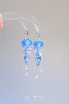 These earrings feature delicate blue glass beads and silver chains, perfectly mimicking the ethereal beauty of jellyfish floating in the ocean. The cascading chains and shimmering beads create a mesmerizing effect with every movement, making these earrings a captivating accessory for any outfit. Ideal for ocean lovers and those who adore statement jewelry. Perfect for beach outings, summer festivals, or as a thoughtful gift for someone who loves the sea. - Width: 3/4" | 1.9cm - Length: 3" | 7.6c Jelly Fish Earrings, Blue Dangle Earrings With Ocean-inspired Style, Ocean-inspired Blue Dangle Earrings, Blue Ocean-inspired Dangle Jewelry, Jellyfish Beads, Floating In The Ocean, Ocean Accessories, Water Earrings, Jellyfish Jewelry