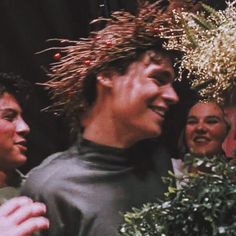 two men are smiling and one is wearing a wreath on his head while the other looks at him