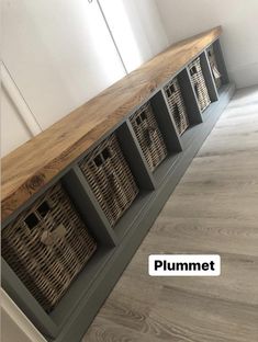 a wooden shelf with baskets on top of it in front of a white wall and wood floor