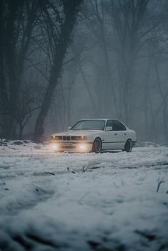 a white car driving down a snow covered road in the middle of winter with headlights on