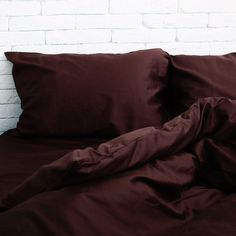 a bed with brown sheets and pillows against a white brick wall in front of it