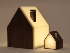 a small wooden house next to a lit candle on a white surface with a light in the shape of a house