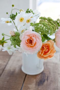 three different colored flowers in a white vase on a wooden table next to a window