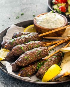 some skewered food on a plate with lemon wedges