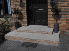 a black door is on the side of a brick building with potted plants in front