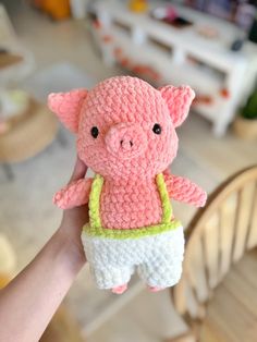 a hand holding a small crocheted pig in shorts and a t - shirt