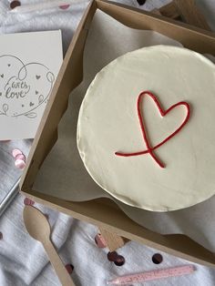 a white cake in a box with a red heart on it and a card next to it