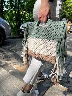 a woman is holding a crocheted bag on the sidewalk