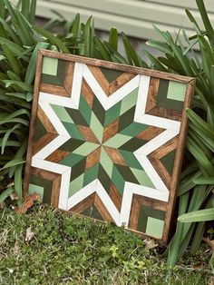 a green and white quilt sitting on the ground in front of some grass with plants